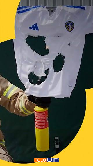 A firefighter holding a badly melted counterfeit white football shirt above a fire extinguisher